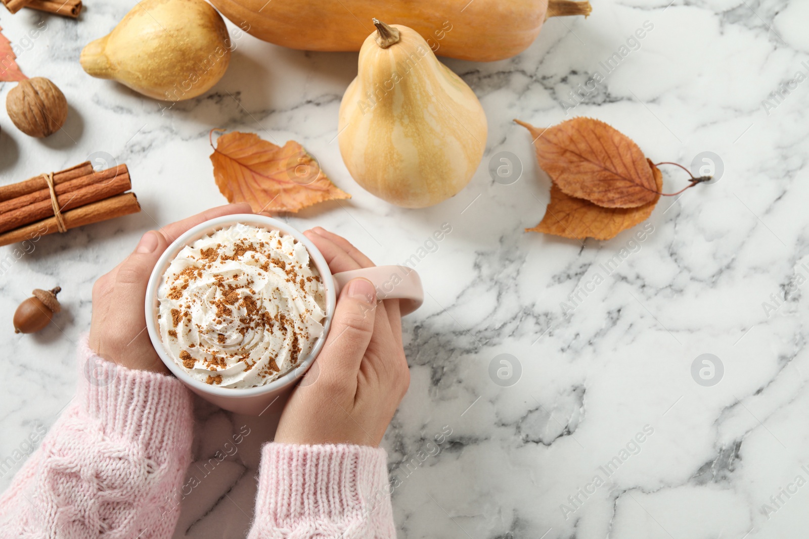 Photo of Woman with cup of tasty pumpkin spice latte at white marble table, top view. Space for text