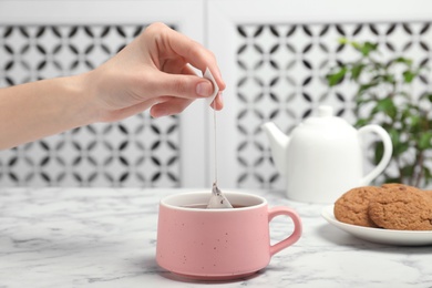 Photo of Woman brewing tea with bag in cup on table, closeup