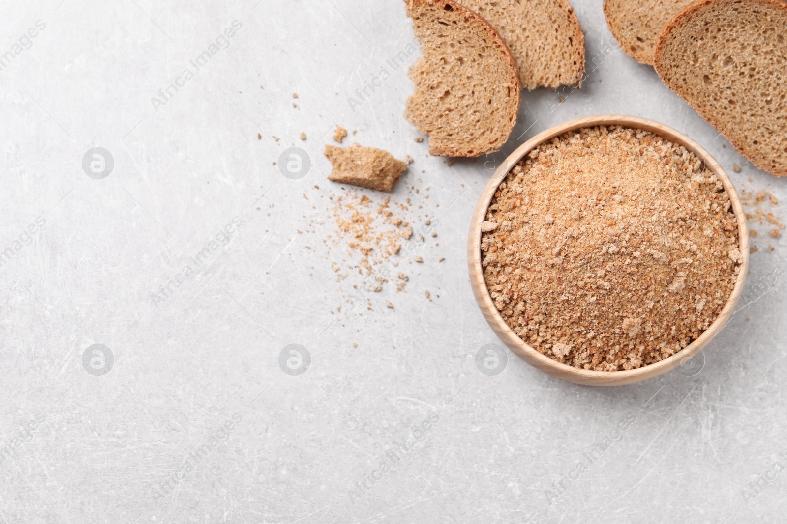 Photo of Fresh bread crumbs in bowl on grey table, flat lay. Space for text