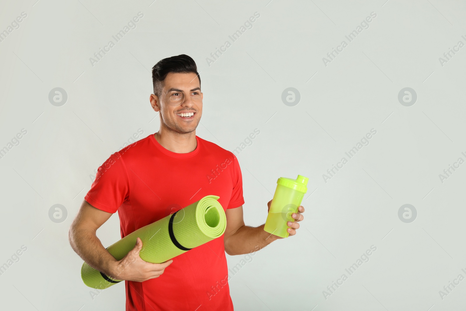 Photo of Handsome man with yoga mat and shaker on light background. Space for text