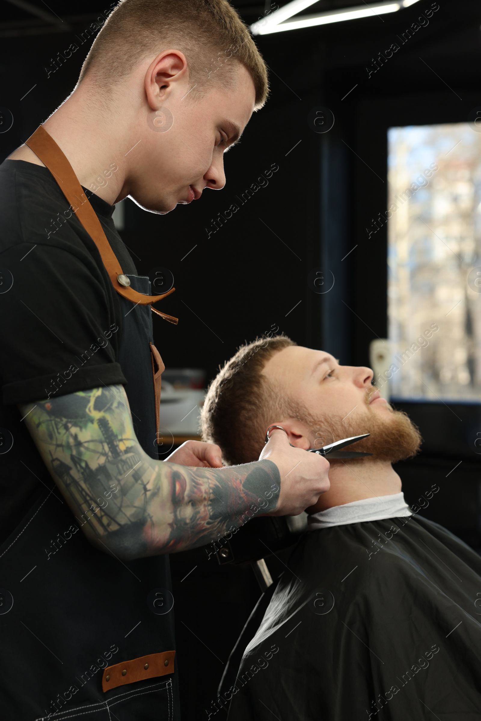 Photo of Professional hairdresser working with bearded client in barbershop