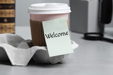 Image of Sticky note with word Welcome attached to paper cup of coffee on office desk