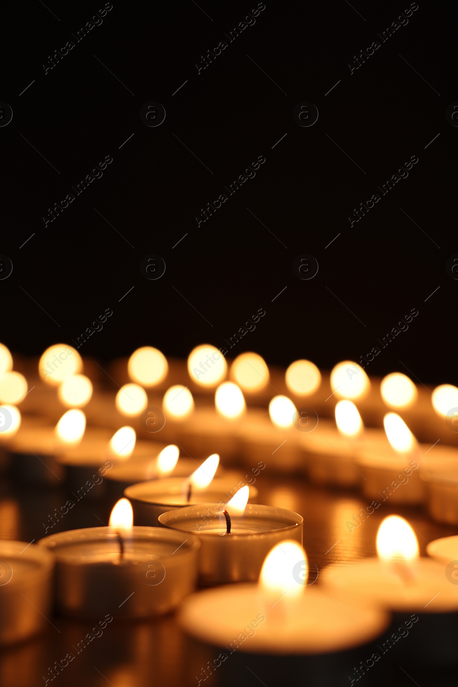 Photo of Burning candles on dark surface against black background