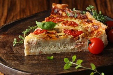 Piece of delicious homemade quiche with prosciutto, tomatoes and greens on serving board, closeup