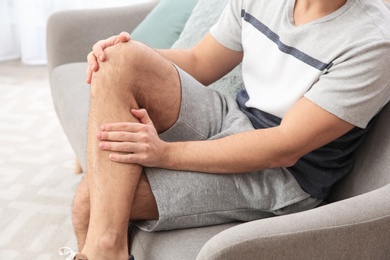 Photo of Man suffering from leg pain at home, closeup