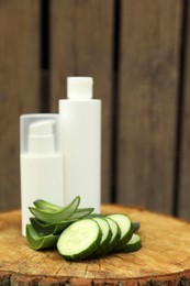 Photo of Bottles of cosmetic products, sliced aloe vera leaves and cucumber on wooden stump