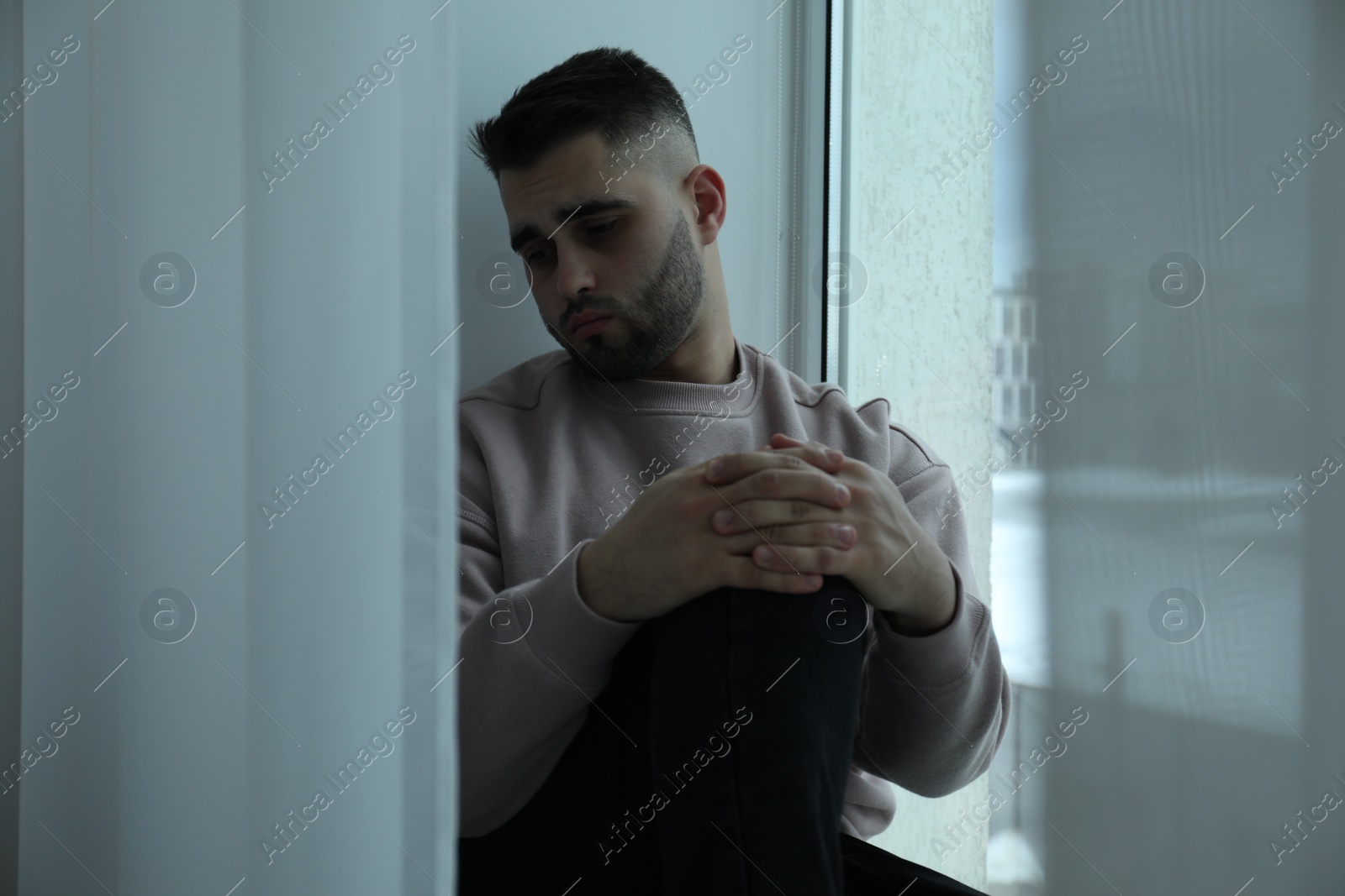 Photo of Sad man sitting near window at home