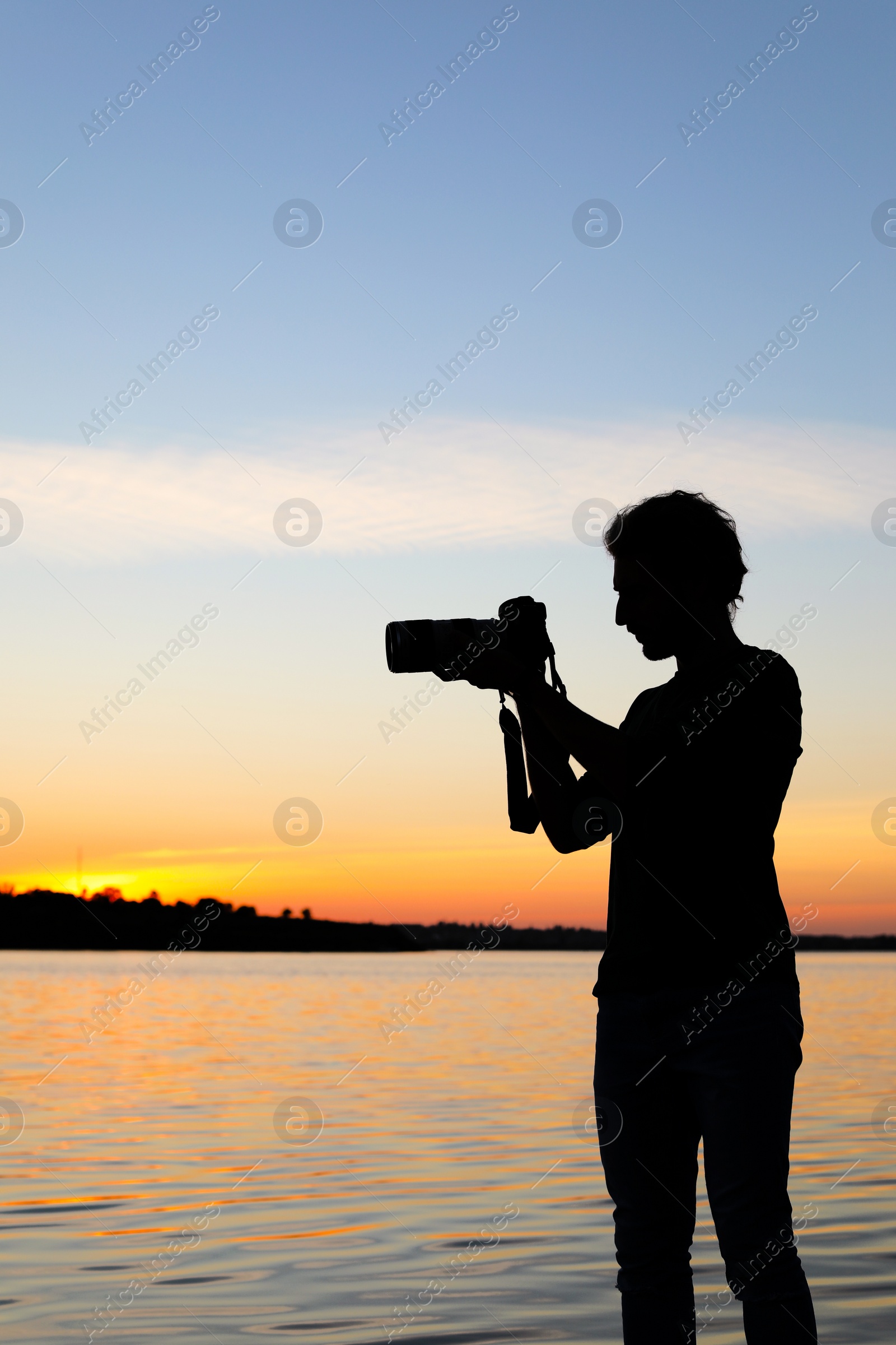Photo of Young male photographer taking photo of riverside sunset with professional camera outdoors