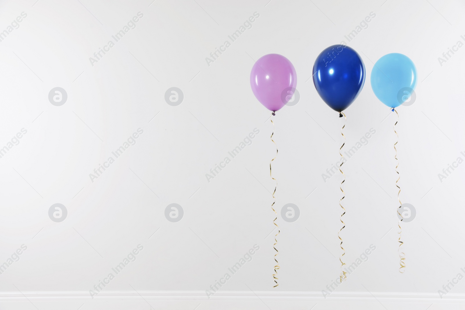 Photo of Different bright balloons against light wall, space for text. Celebration time