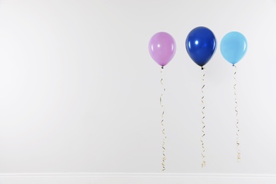 Photo of Different bright balloons against light wall, space for text. Celebration time