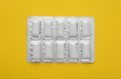 Photo of Blister of tasty chewing gums on yellow background, top view