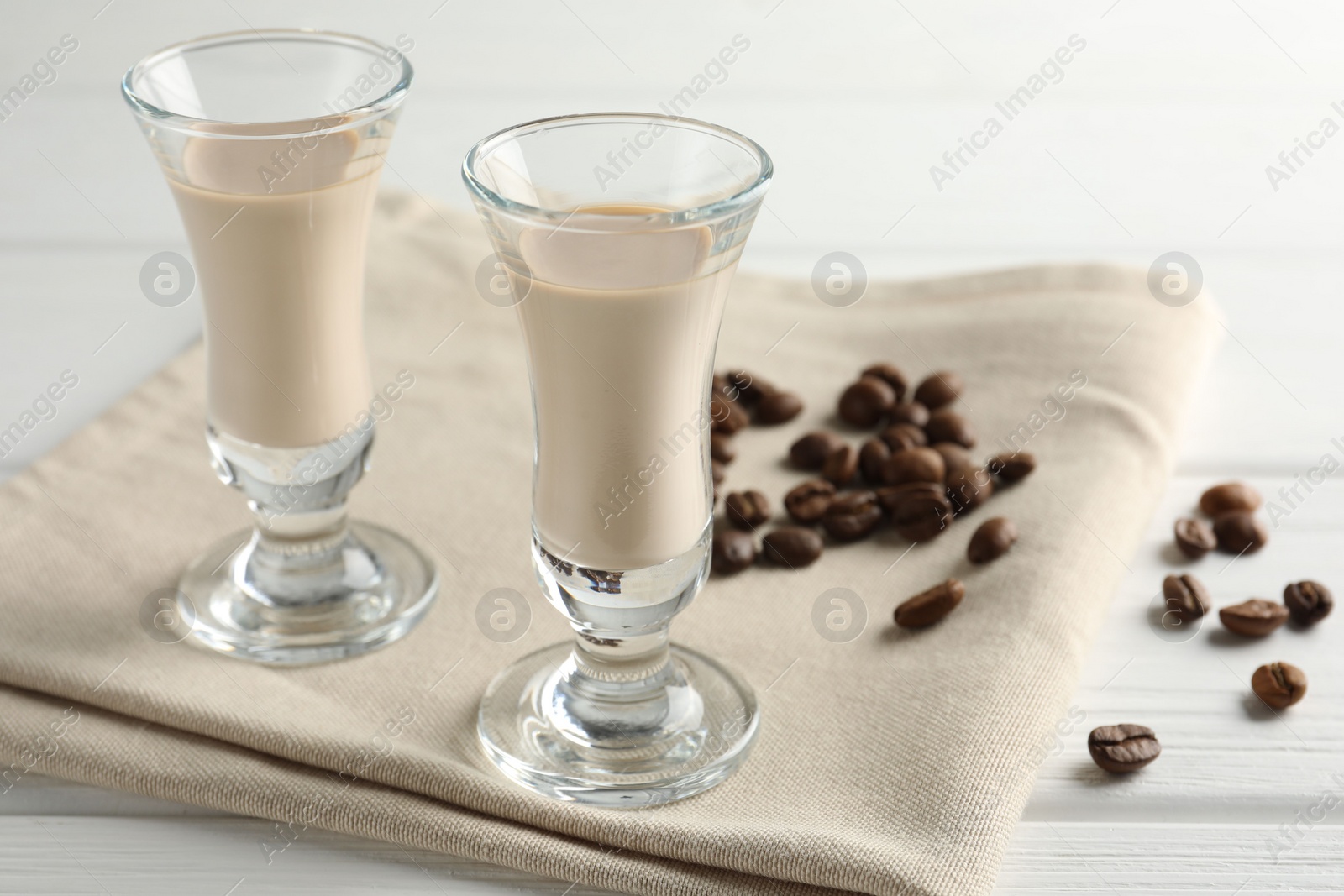 Photo of Coffee cream liqueur in glasses and beans on white wooden table