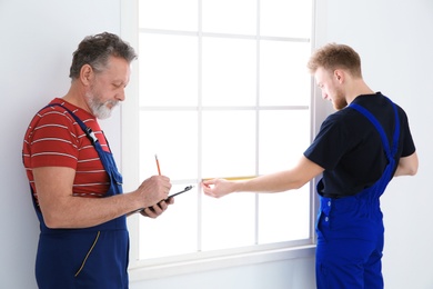 Service men measuring window for installation indoors