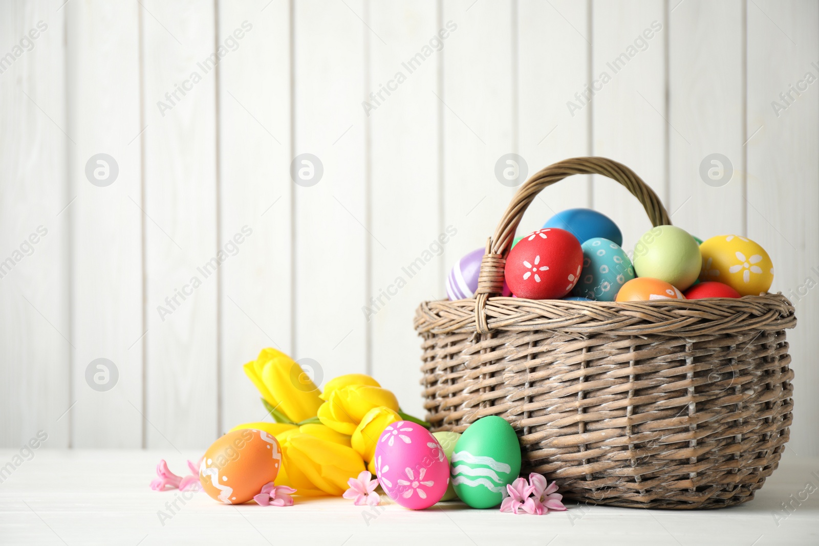 Photo of Colorful Easter eggs and flowers on white wooden table. Space for text