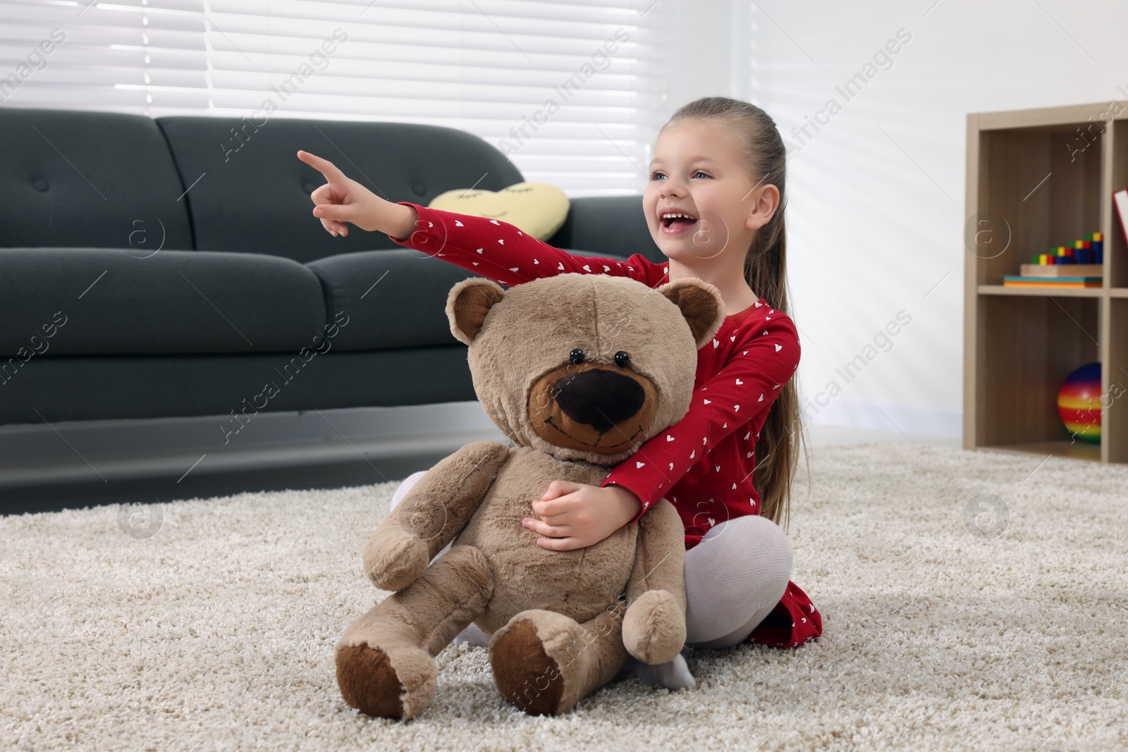 Photo of Cute little girl playing with teddy bear at home