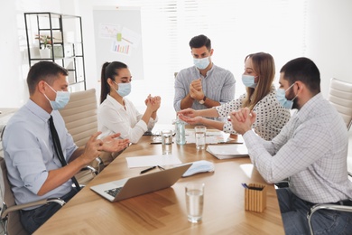 Photo of Coworkers with protective masks using hand sanitizer in office. Business meeting during COVID-19 pandemic