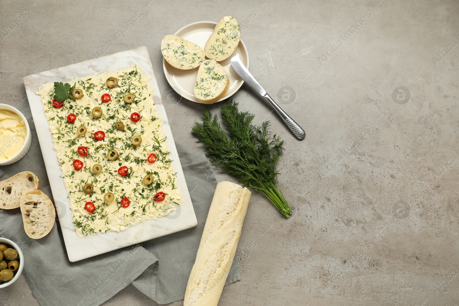 Photo of Fresh butter board with cut olives, dill, bread and knife on grey table, flat lay. Space for text