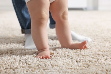 Photo of Mother supporting her baby son while he learning to walk on carpet at home, closeup