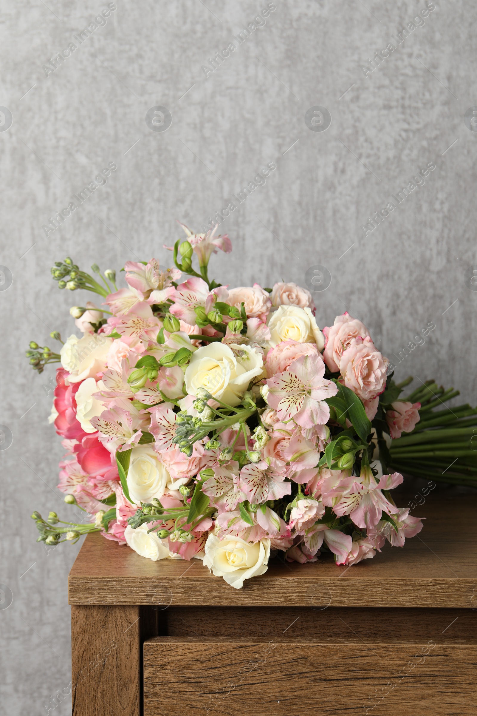 Photo of Beautiful bouquet of fresh flowers on wooden table near grey wall