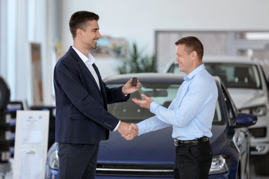 Photo of Young salesman working with client in car dealership