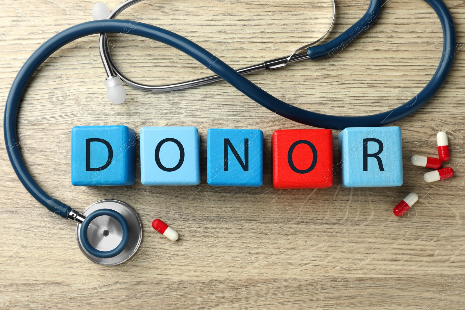 Photo of Word Donor made of cubes, stethoscope and pills on wooden table, flat lay