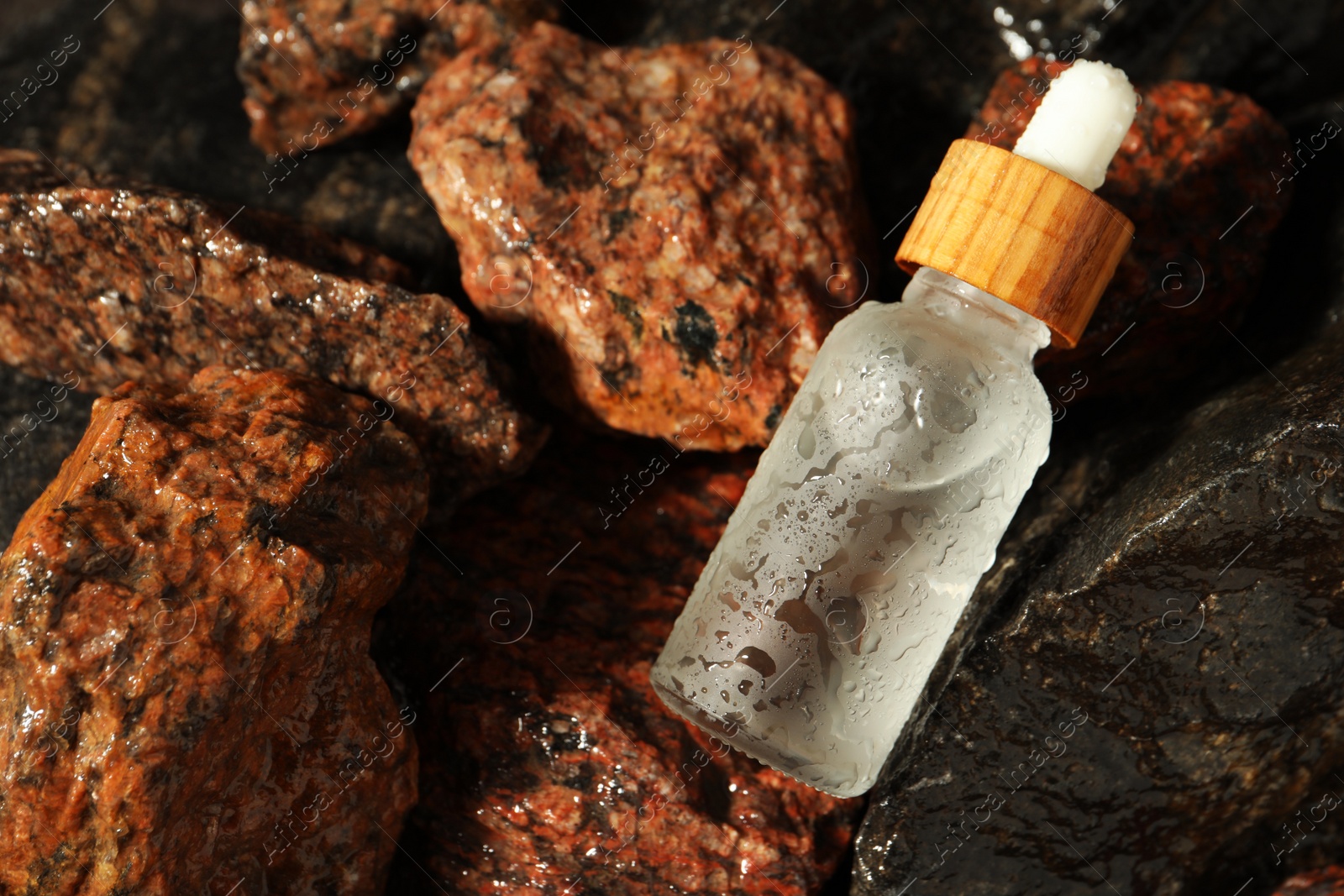 Photo of Bottle of face serum on wet stones, top view. Space for text