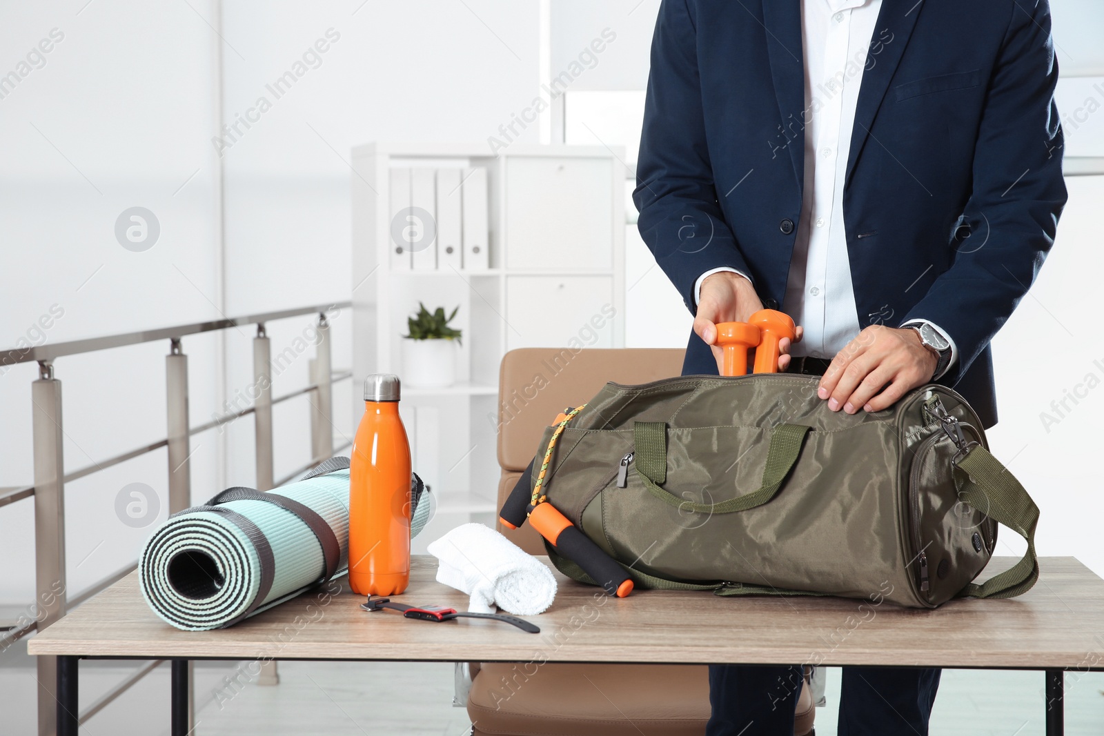 Photo of Businessman packing sports stuff for training into bag in office, closeup