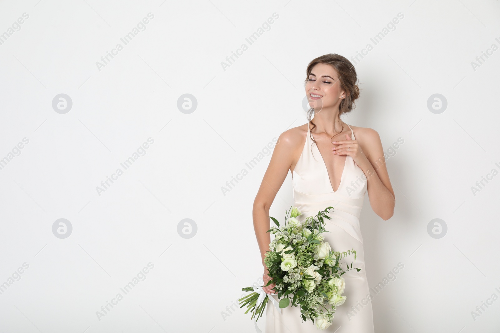 Photo of Young bride wearing wedding dress with beautiful bouquet on light background. Space for text