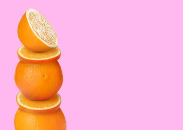 Stacked cut and whole oranges on pink yellow background, space for text