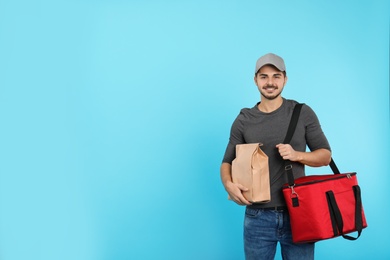 Photo of Young courier with thermo bag and paper package on color background, space for text. Food delivery service