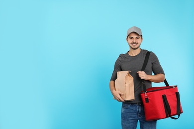 Young courier with thermo bag and paper package on color background, space for text. Food delivery service