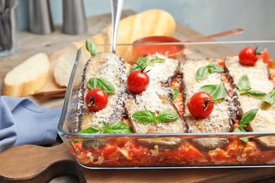 Photo of Baked eggplant with tomatoes, cheese and basil in dishware on table, closeup