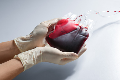Woman holding blood for transfusion on light background, closeup. Donation concept