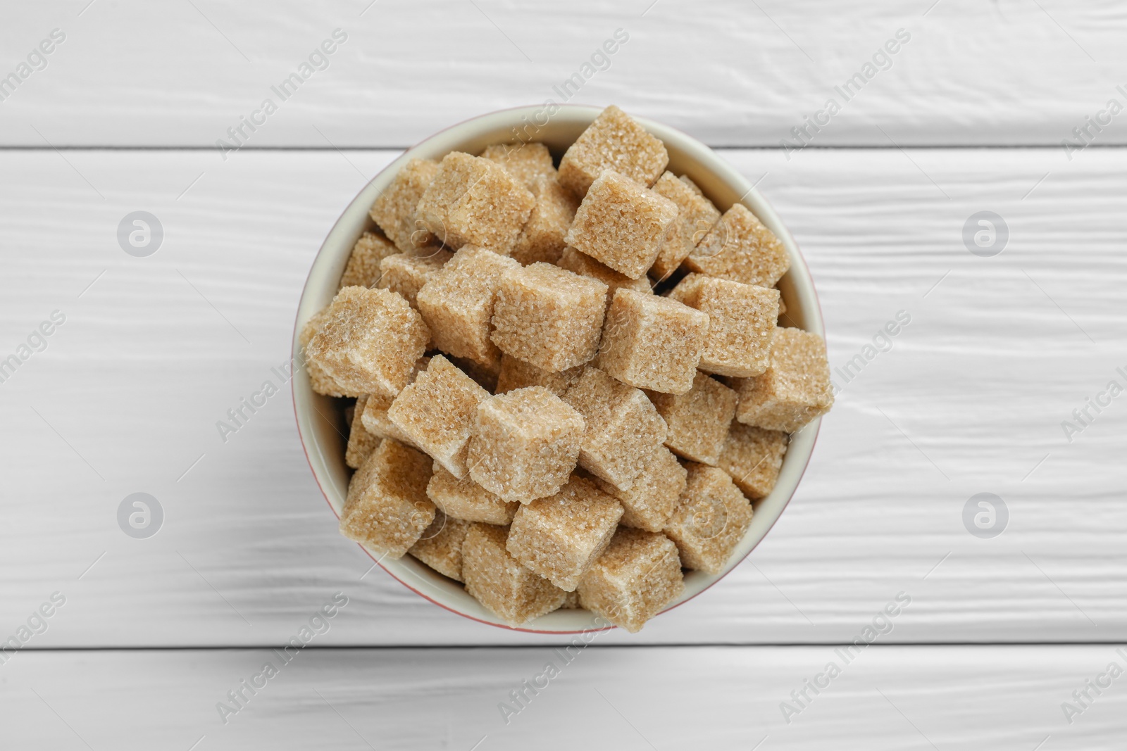 Photo of Brown sugar cubes in bowl on white wooden table, top view