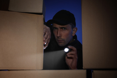Security guard with flashlight looking through pile of cardboard boxes in dark room