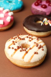 Photo of Sweet tasty glazed donuts on brown background, closeup