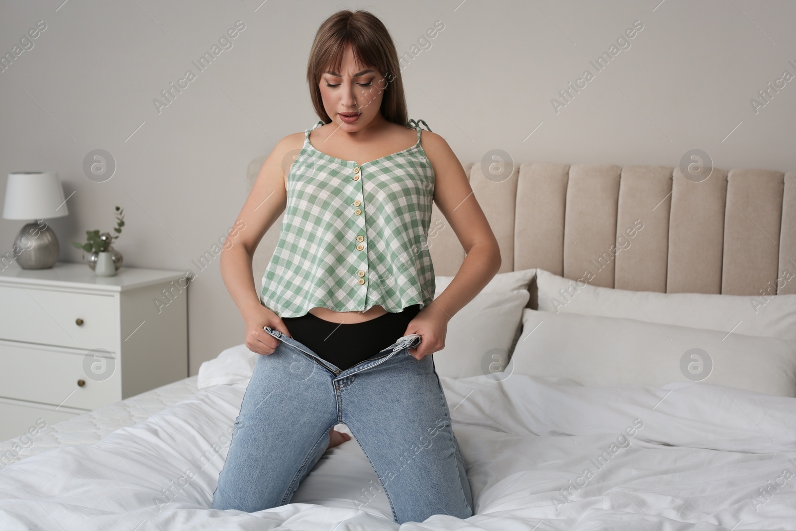 Photo of Young woman trying to squeeze into tight jeans on bed at home. Space for text