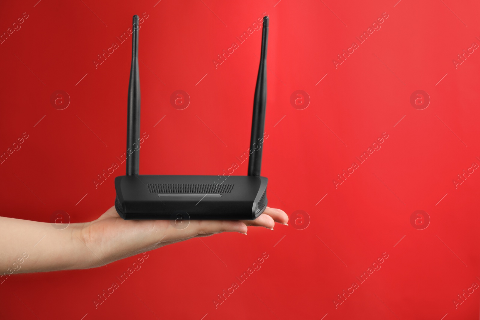 Photo of Woman holding modern Wi-Fi router on red background, closeup. Space for text