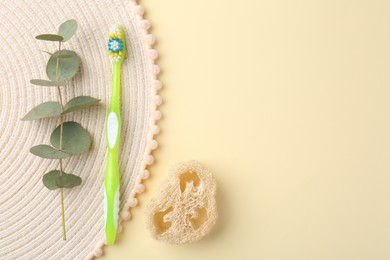 Photo of Plastic toothbrush, eucalyptus branch and loofah on pale yellow background, flat lay. Space for text