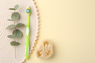 Plastic toothbrush, eucalyptus branch and loofah on pale yellow background, flat lay. Space for text