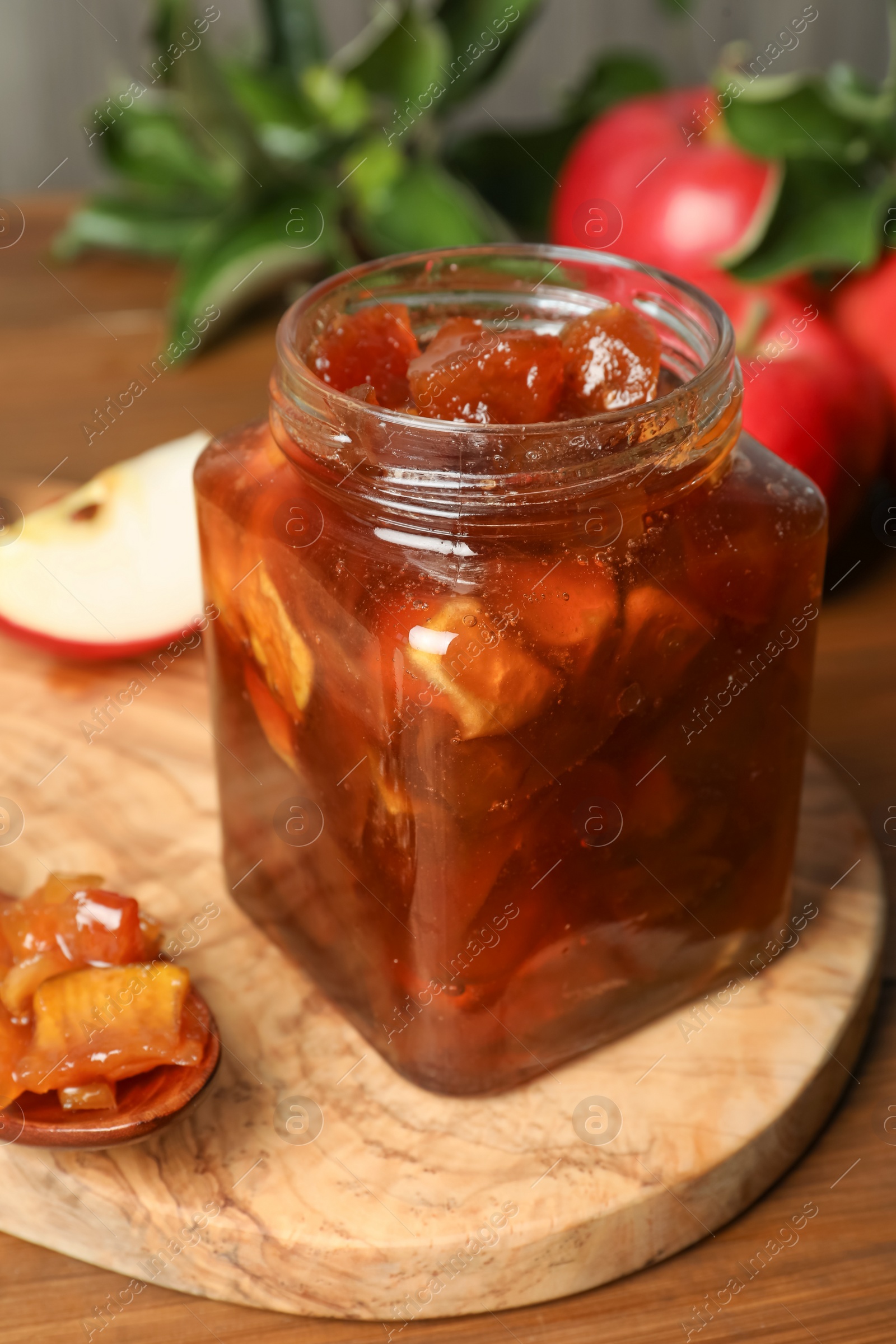 Photo of Tasty apple jam in glass jar on wooden table, closeup