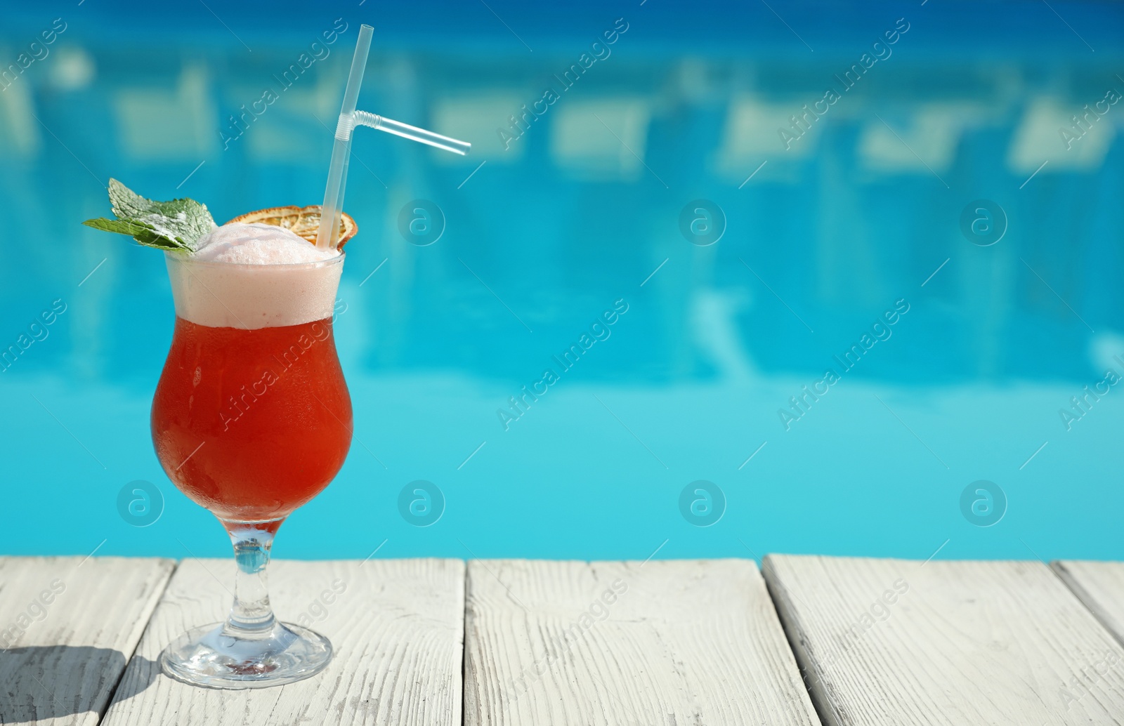 Photo of Refreshing cocktail near swimming pool outdoors on sunny day. Space for text