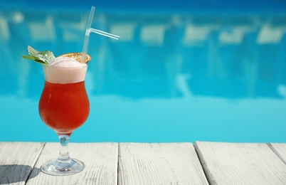 Refreshing cocktail near swimming pool outdoors on sunny day. Space for text