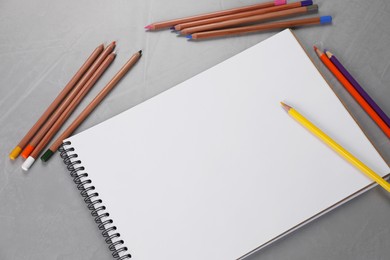 Photo of Empty sketchbook and colorful pencils on grey textured table, flat lay