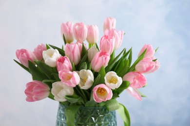 Photo of Beautiful bouquet of tulips in glass vase against light background