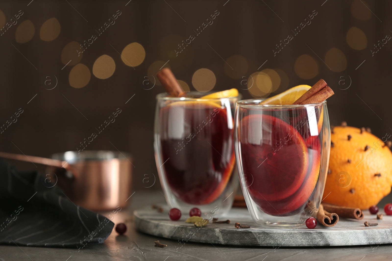 Photo of Glasses of tasty mulled wine on grey table against festive lights