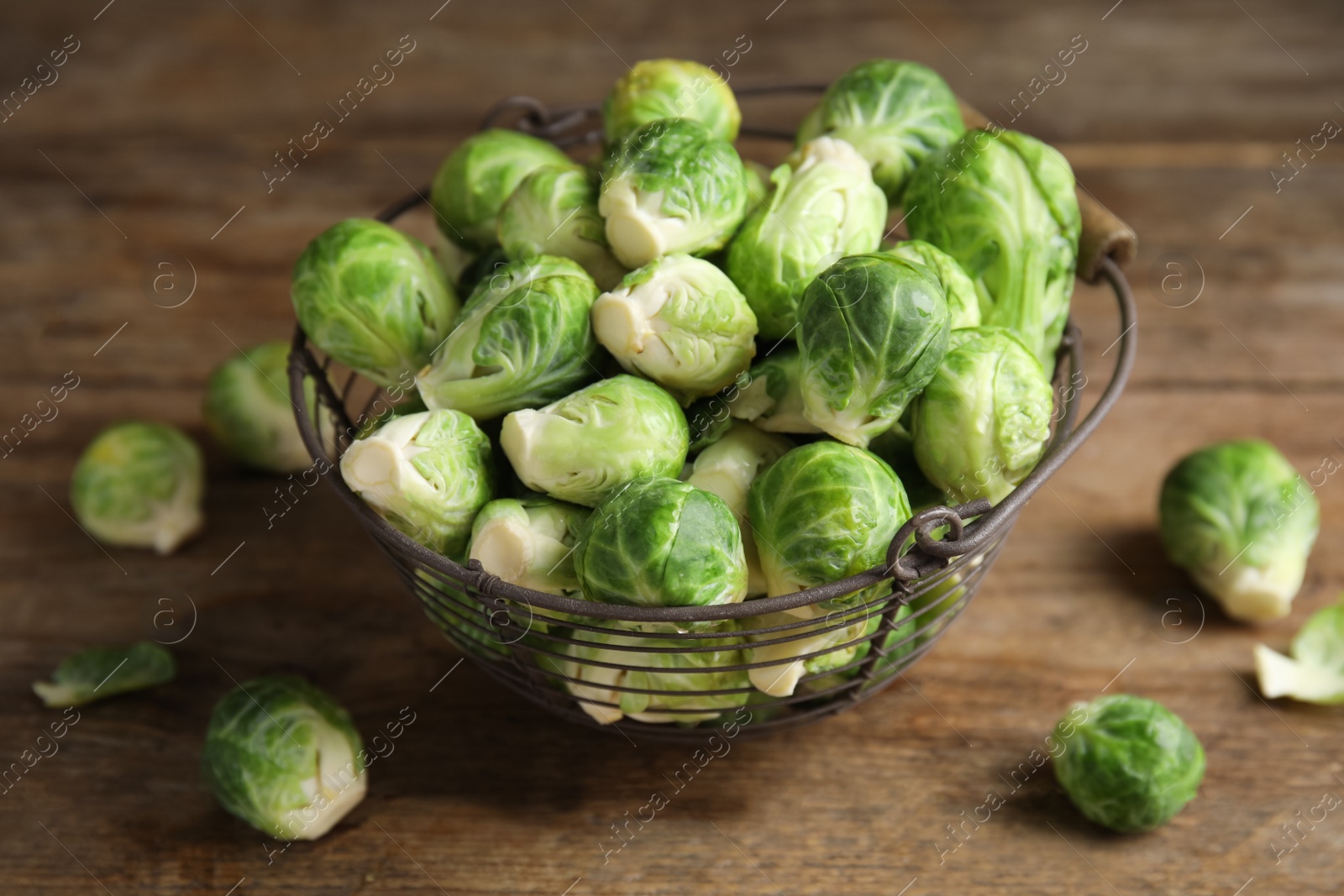 Photo of Metal basket with fresh Brussels sprouts on wooden table, closeup