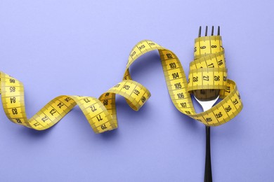 Photo of Fork with measuring tape on violet background, top view. Diet concept