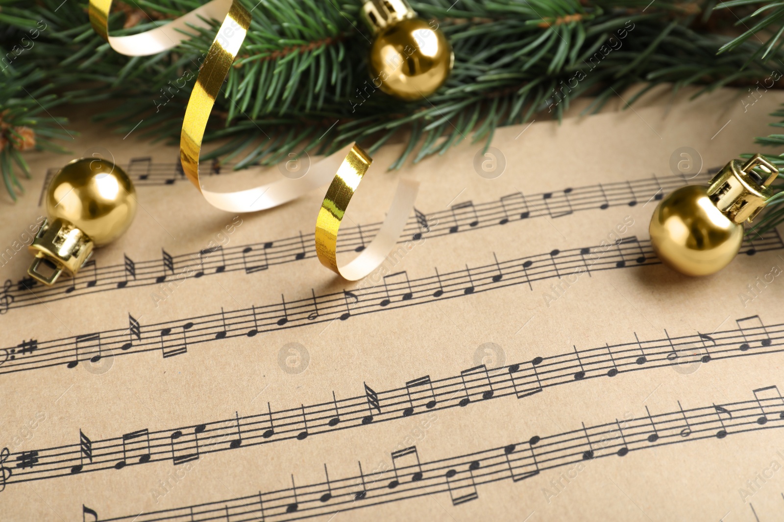 Photo of Fir branches, golden streamer and balls on Christmas music sheets, closeup