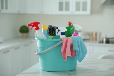 Photo of Plastic bucket with different cleaning supplies on table in kitchen